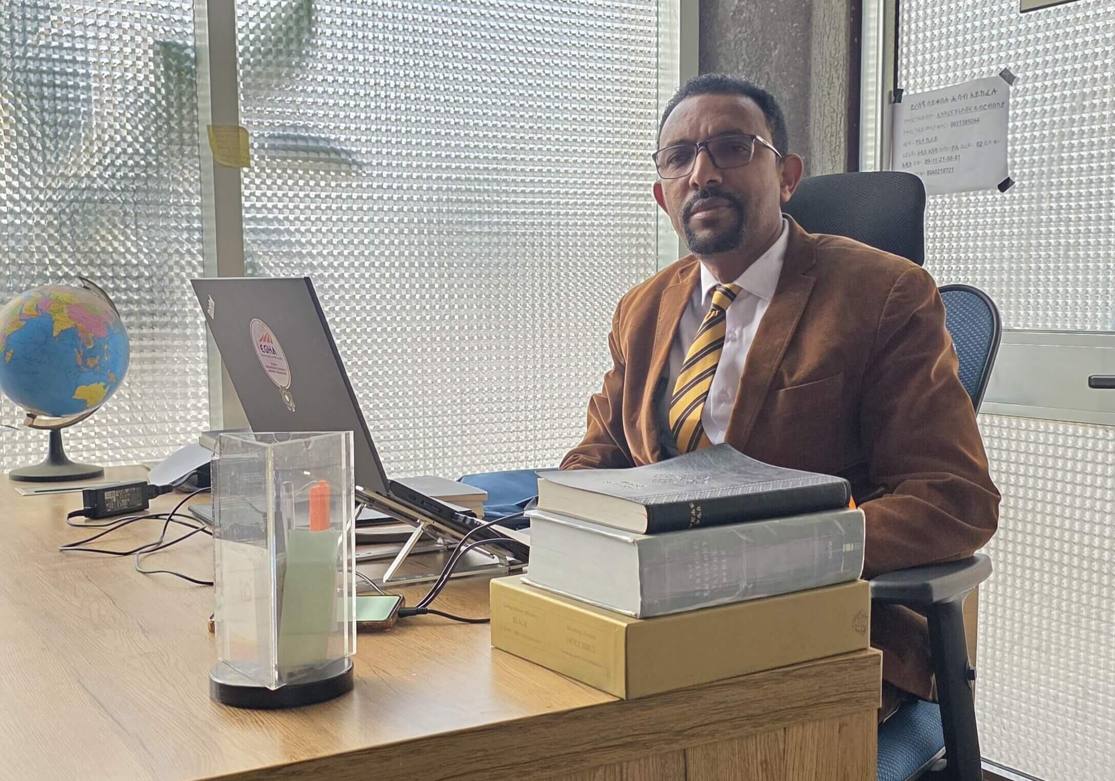 GASHAHUN NEMOMSA sits at his desk with books in front of him